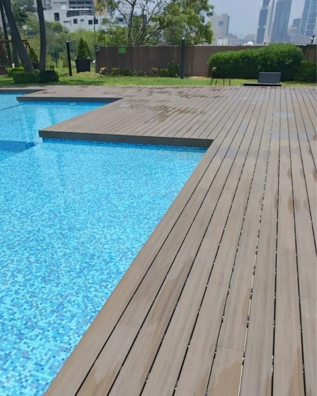 Deck WPC tono madera alrededor de una alberca en una terraza con jardín y torres de la ciudad al fondo