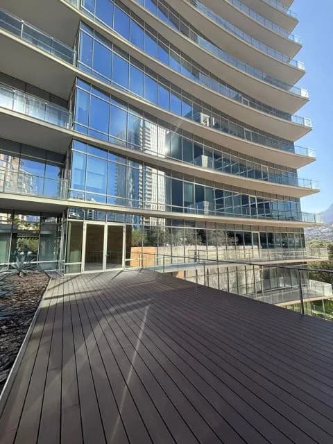 Terraza de deck WPC tono café al pie de un edificio de cristal con balcones, bajo cielo azul