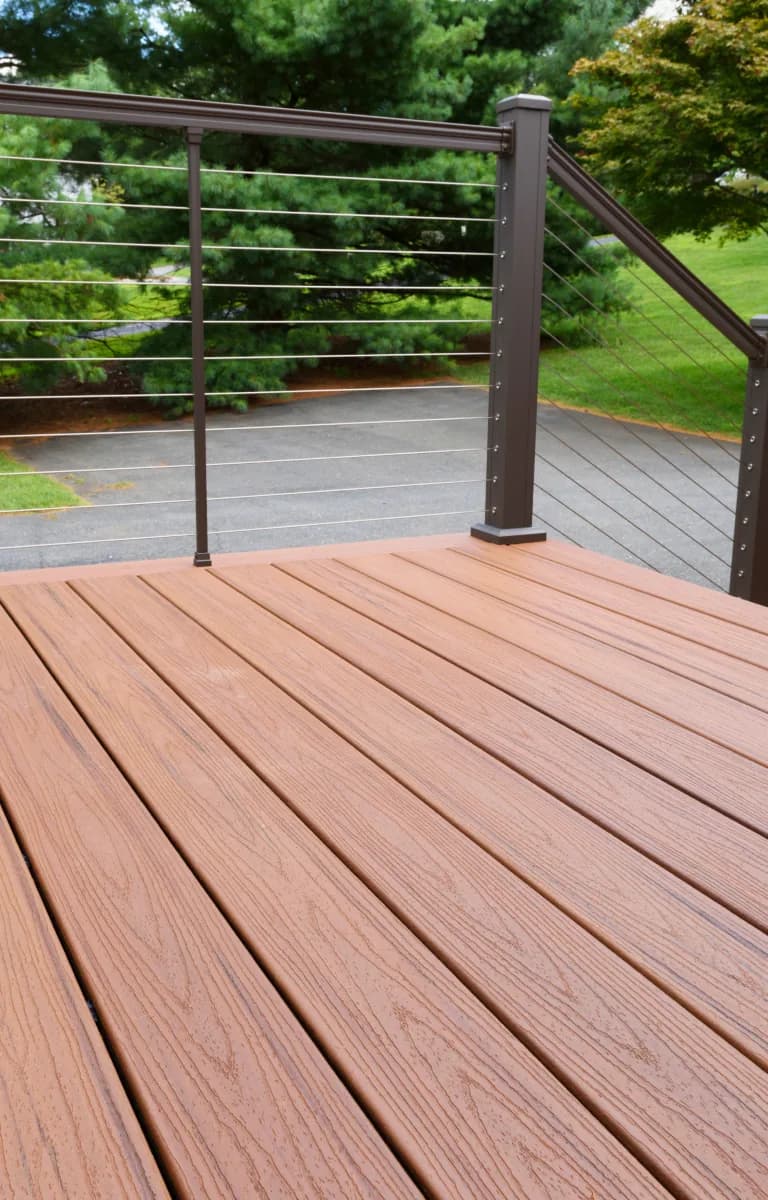 Brown WPC decking on a terrace with cable railing and pine trees in the garden behind