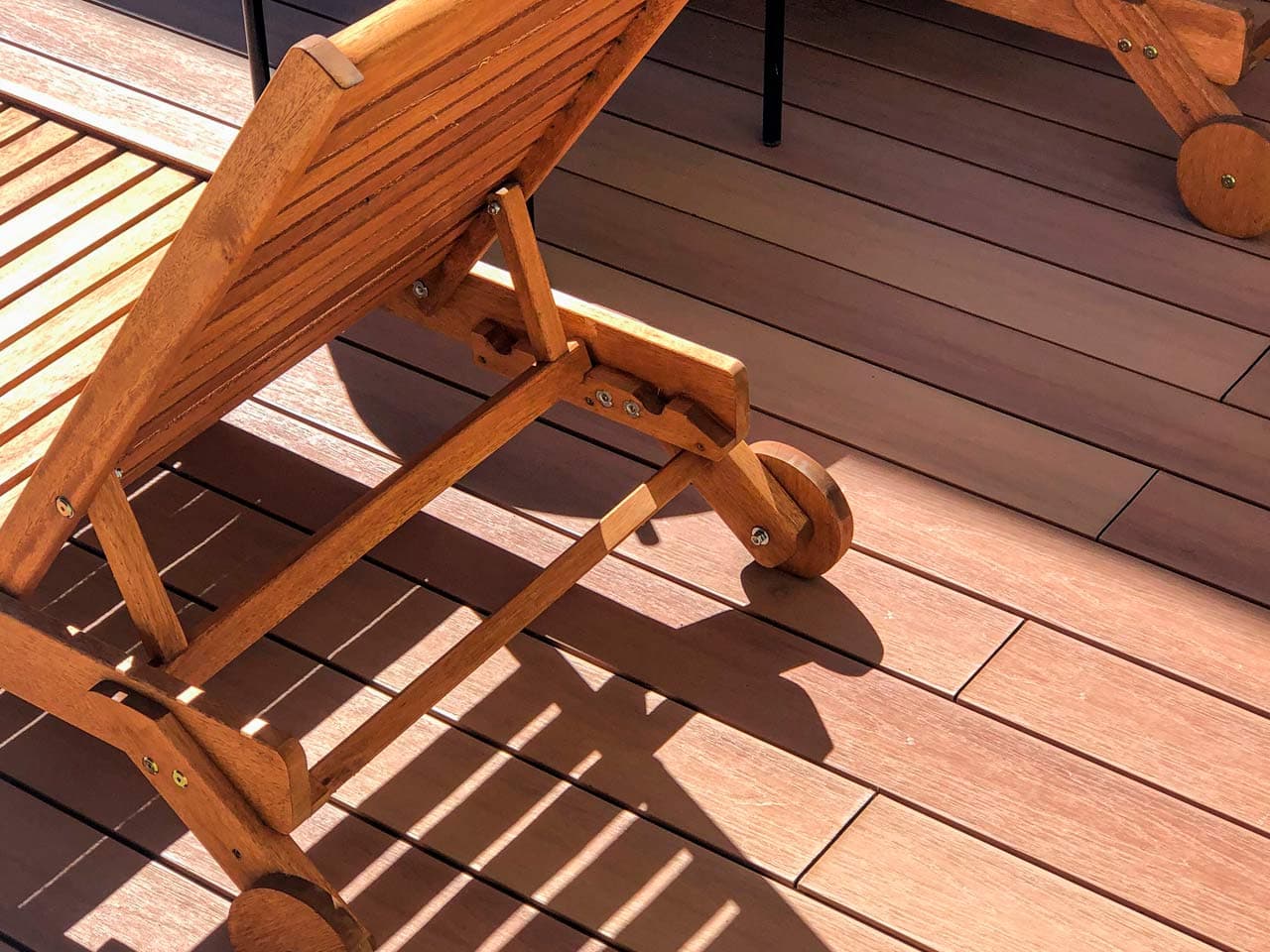 Wooden lounger casting its shadow on a sunlit WPC deck