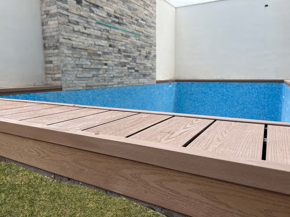 Pool edge finished with light WPC decking next to a stone wall