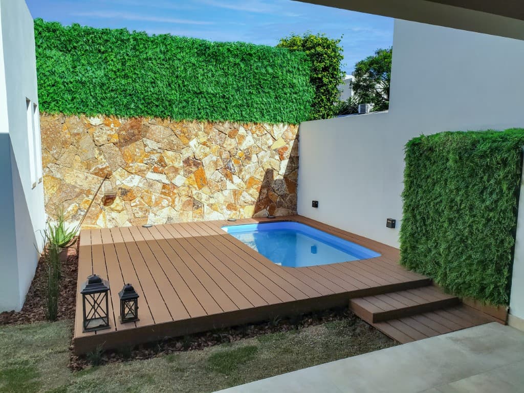 Small pool surrounded by WPC decking, with a stone wall, a green wall and lanterns