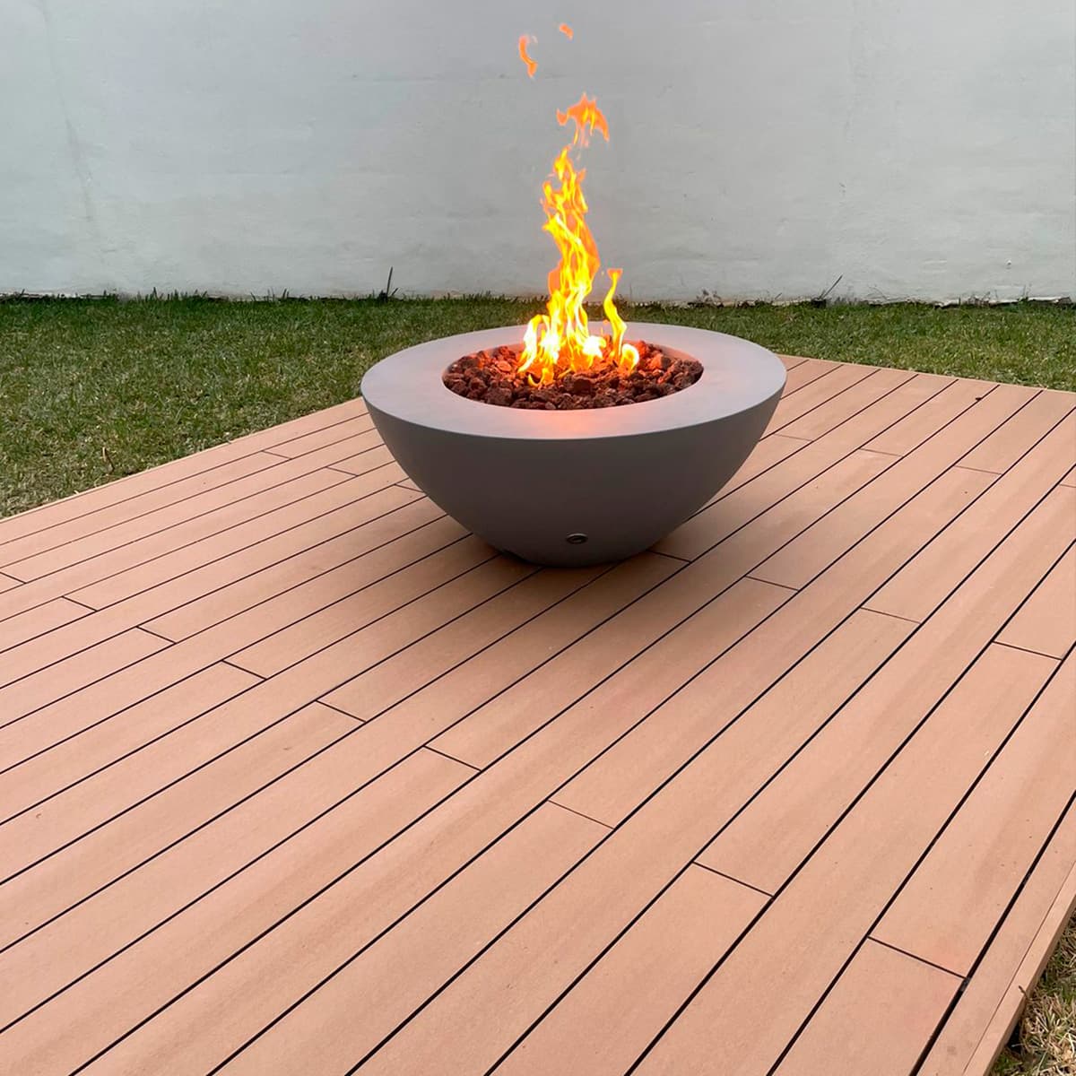 Lit concrete fire bowl on a WPC deck platform in the garden