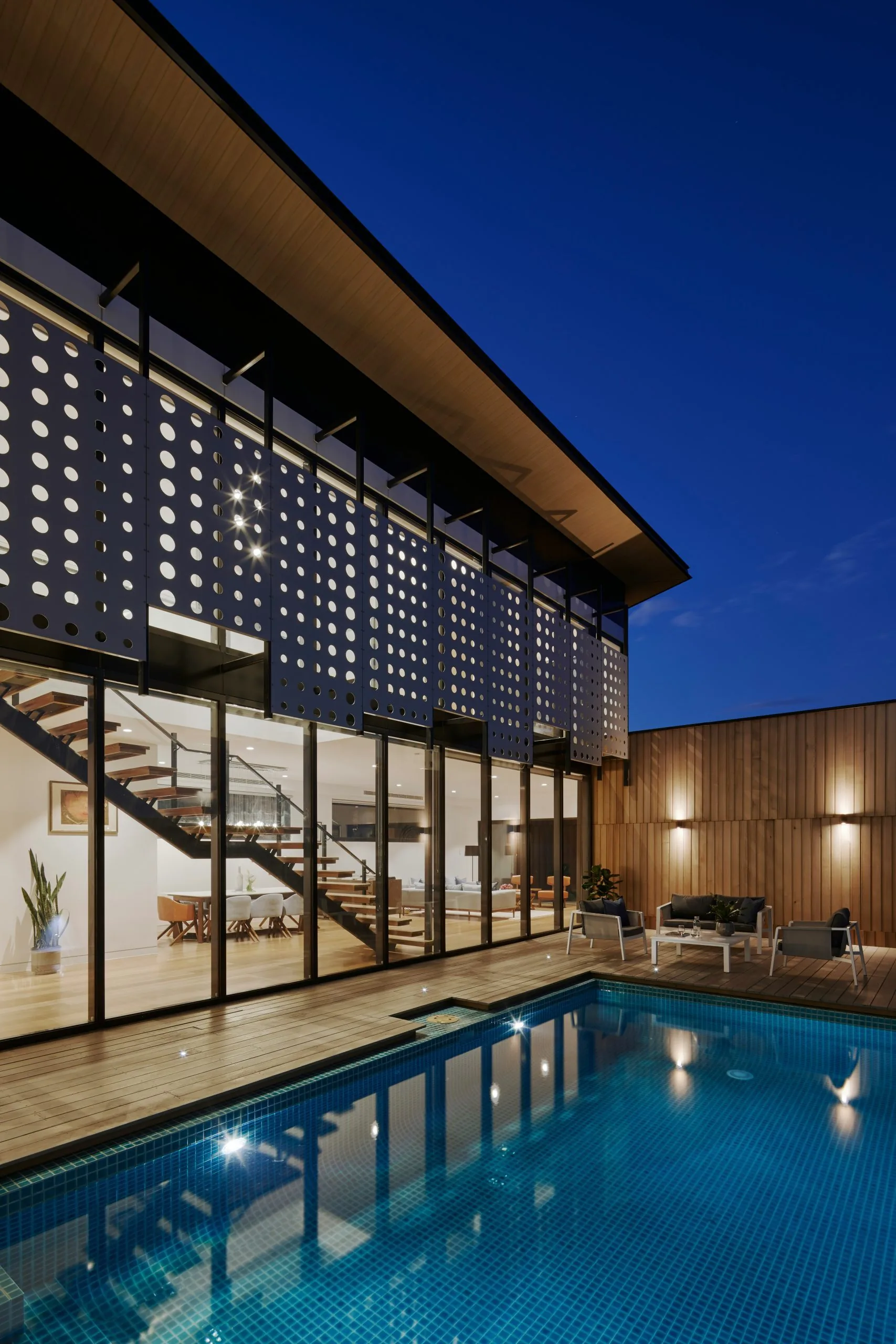 Modern house at night with a slatted screen facade, a lit pool and WPC decking