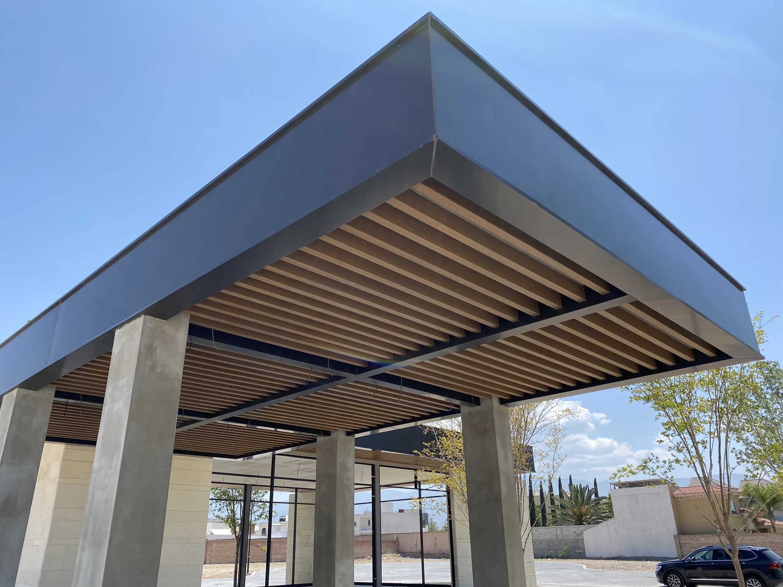 Pérgola exterior con techo de lamas de WPC sobre estructura metálica, vista desde abajo contra el cielo