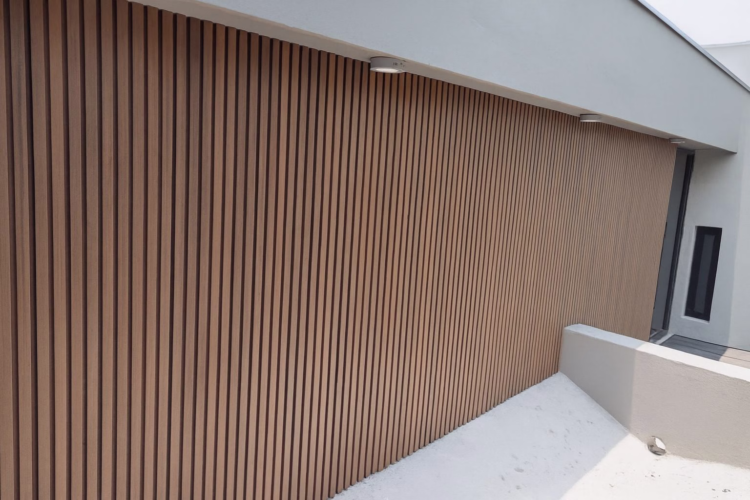 Vertical wood-tone WPC grooved panel wall with a ceiling light