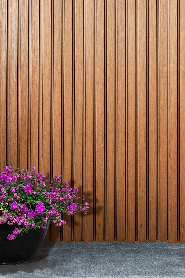 Vertical wood-tone WPC grooved panel wall next to a plant with purple flowers
