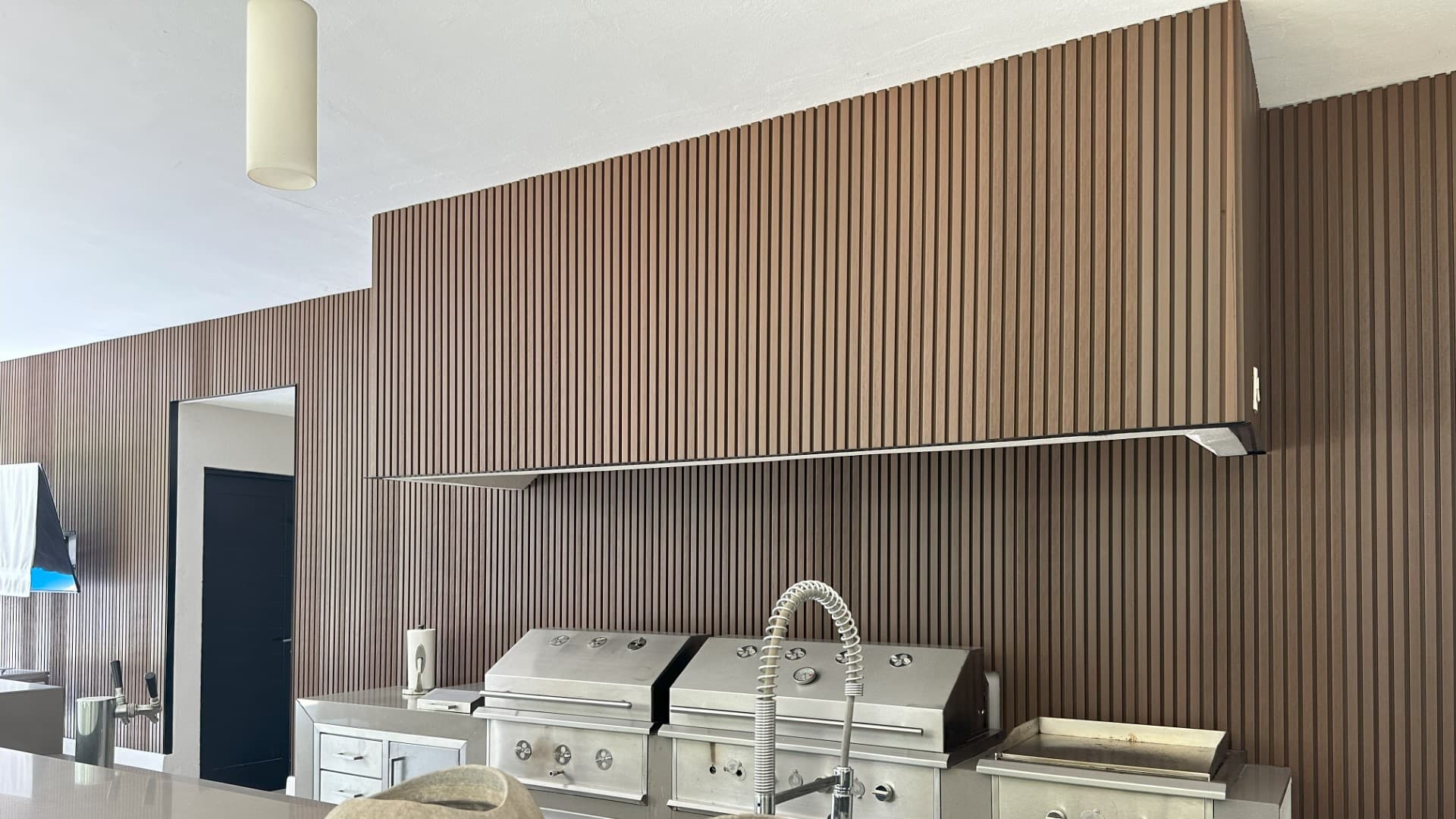 Outdoor kitchen with stainless steel grills in front of a wood-tone WPC grooved panel wall