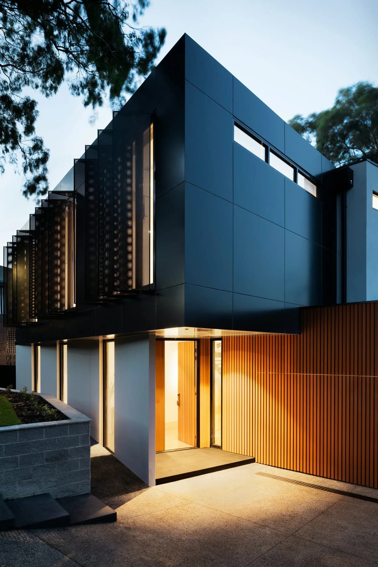 Modern facade at dusk with a lit wood-tone WPC grooved panel wall next to the entrance