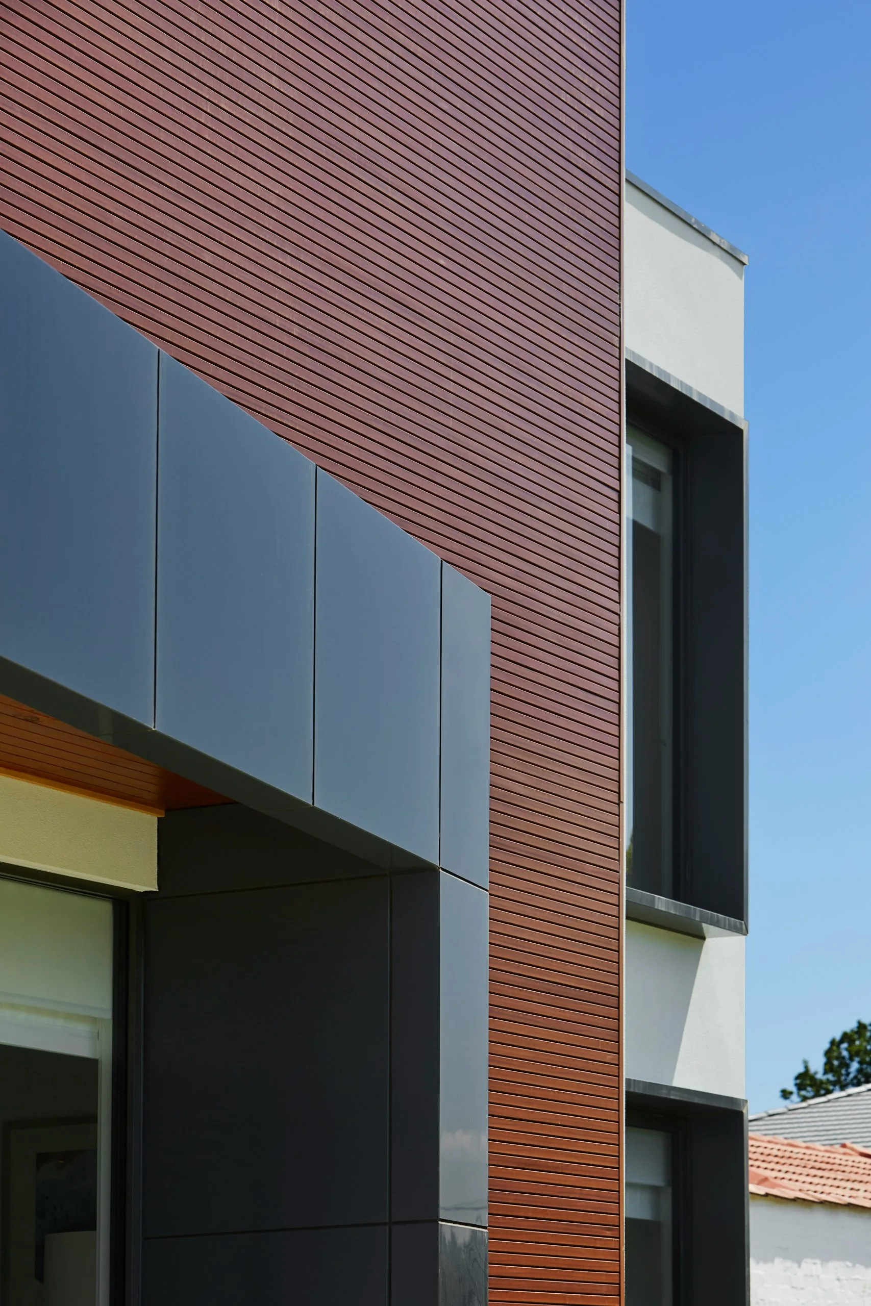 Facade detail with horizontal reddish WPC grooved panel next to gray panels