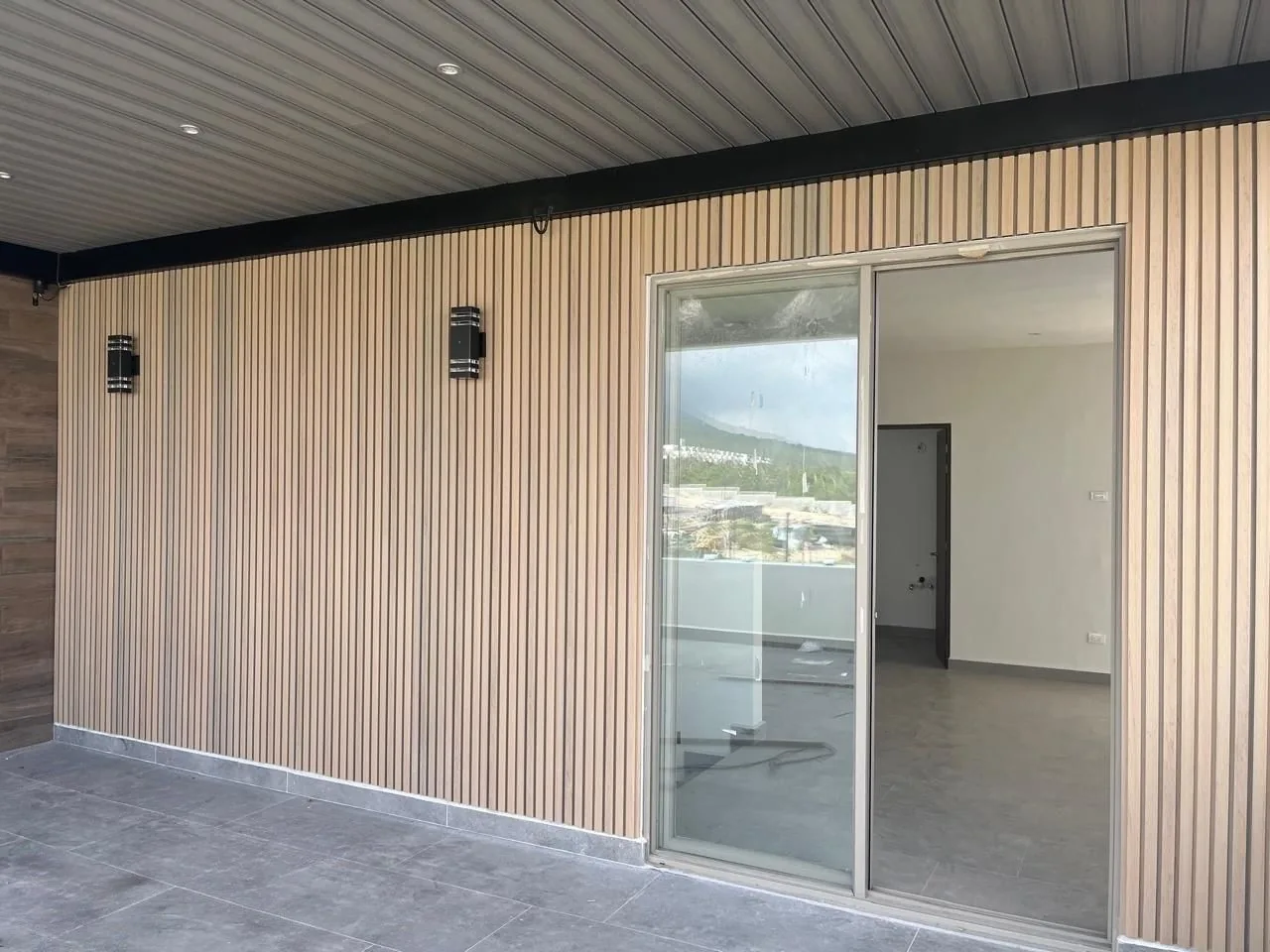 Muro de terraza revestido de lambrín WPC vertical en tono claro, con un cancel corredizo de cristal