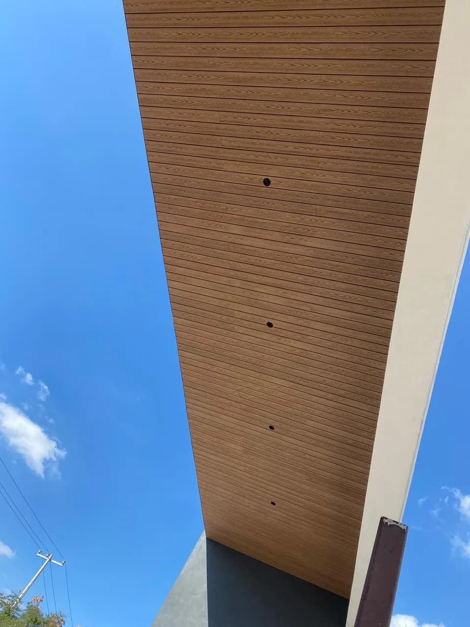 Strip of wood-tone WPC soffit seen from below against a blue sky