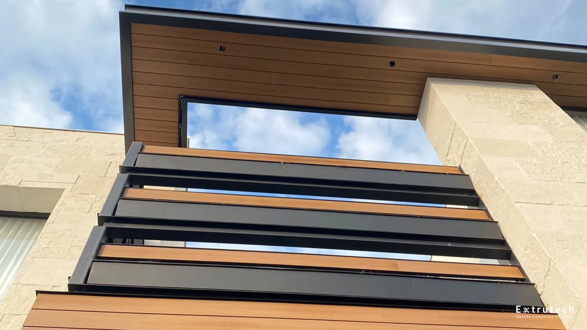 Wood-tone WPC cladding over a window, with dark beams and a cloudy sky