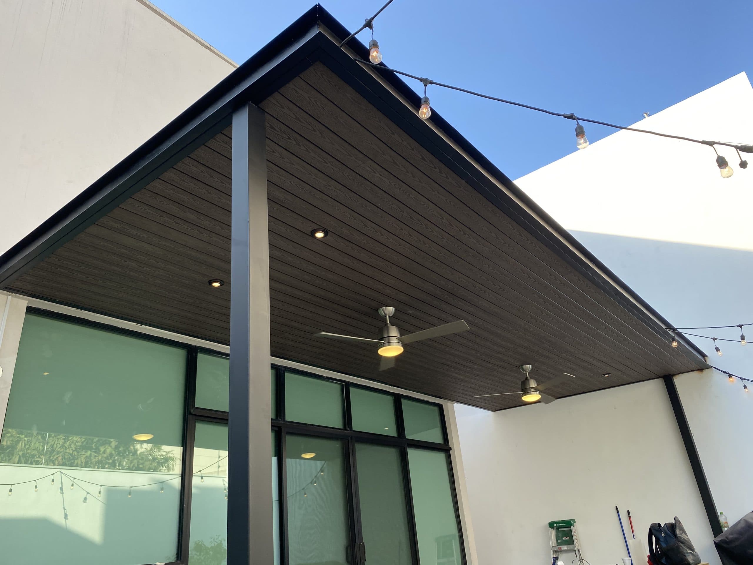 Patio with a gabled ceiling of dark WPC cladding, ceiling fans and large windows