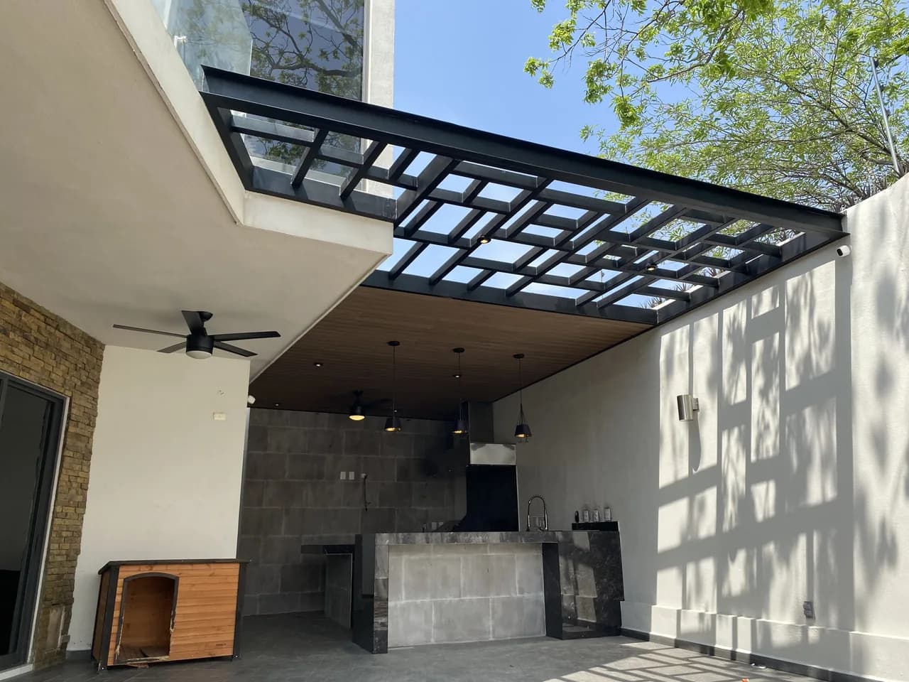 Covered patio with a WPC cladding ceiling, a glass pergola, an outdoor kitchen and a ceiling fan