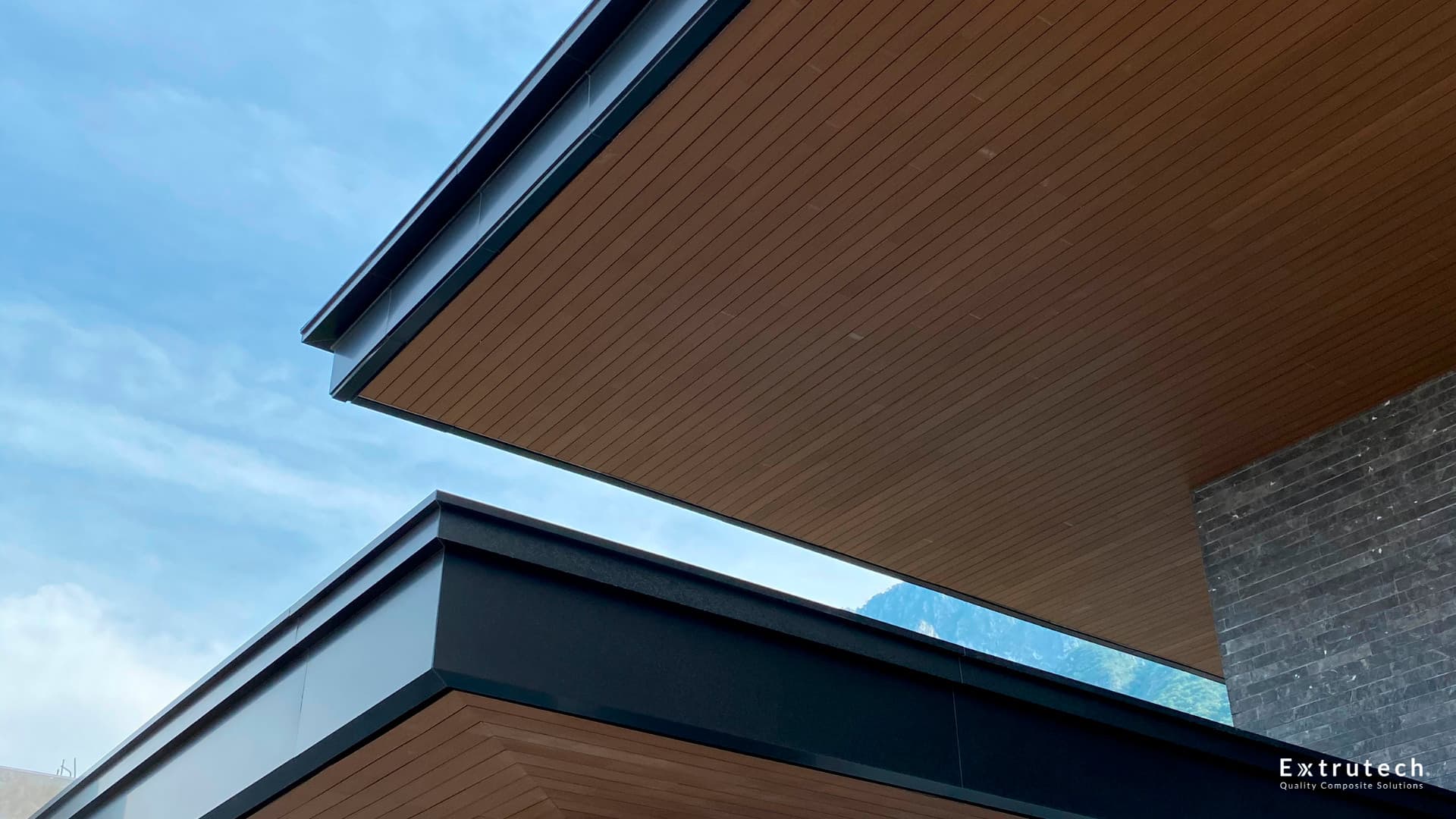 Two overhangs with wood-tone WPC soffits against the sky