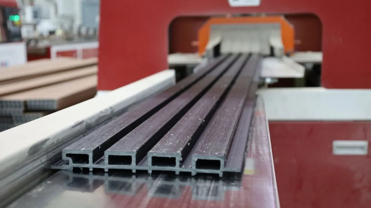 Perfiles de lambrín WPC recién cortados en la línea de la planta de Extrutech, vistos de canto con sus cámaras huecas