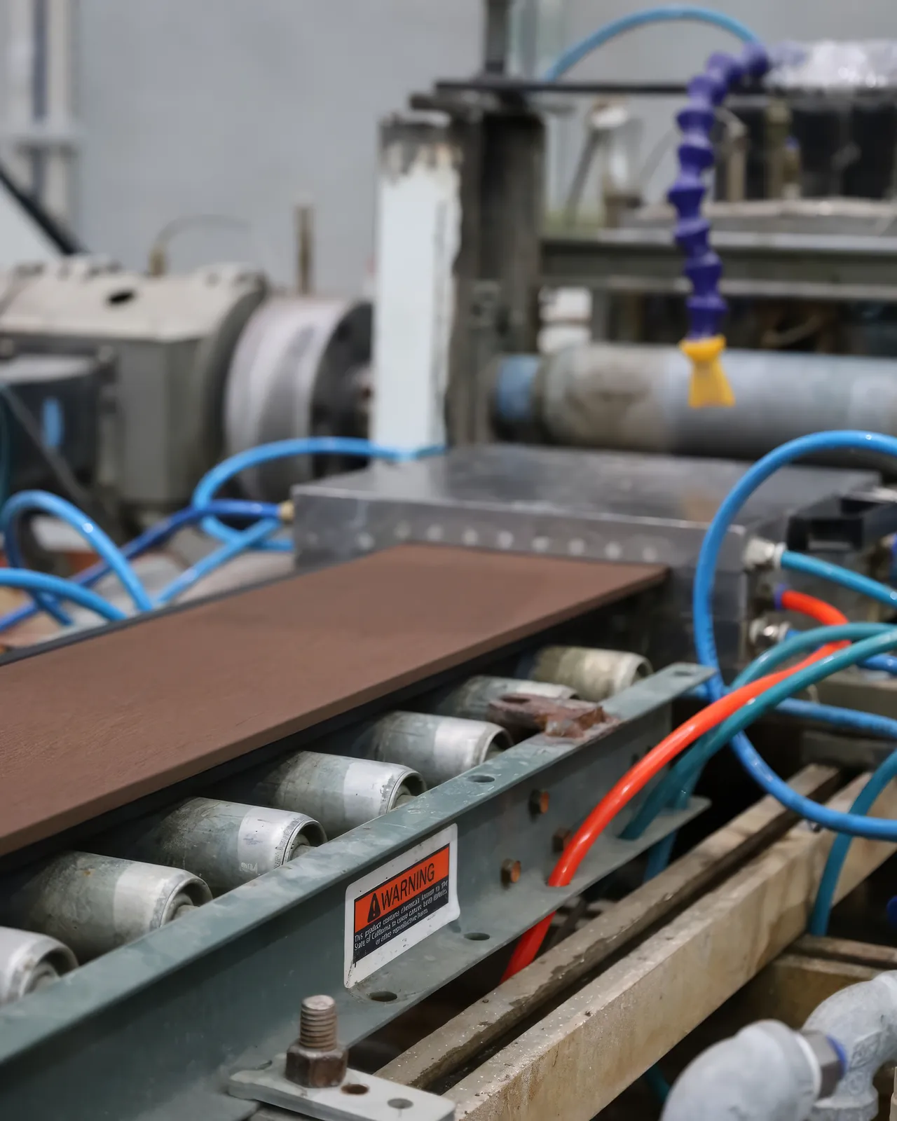 Perfil de WPC recién extruido avanzando sobre los rodillos de la línea en la planta de Extrutech, entre mangueras de aire y agua