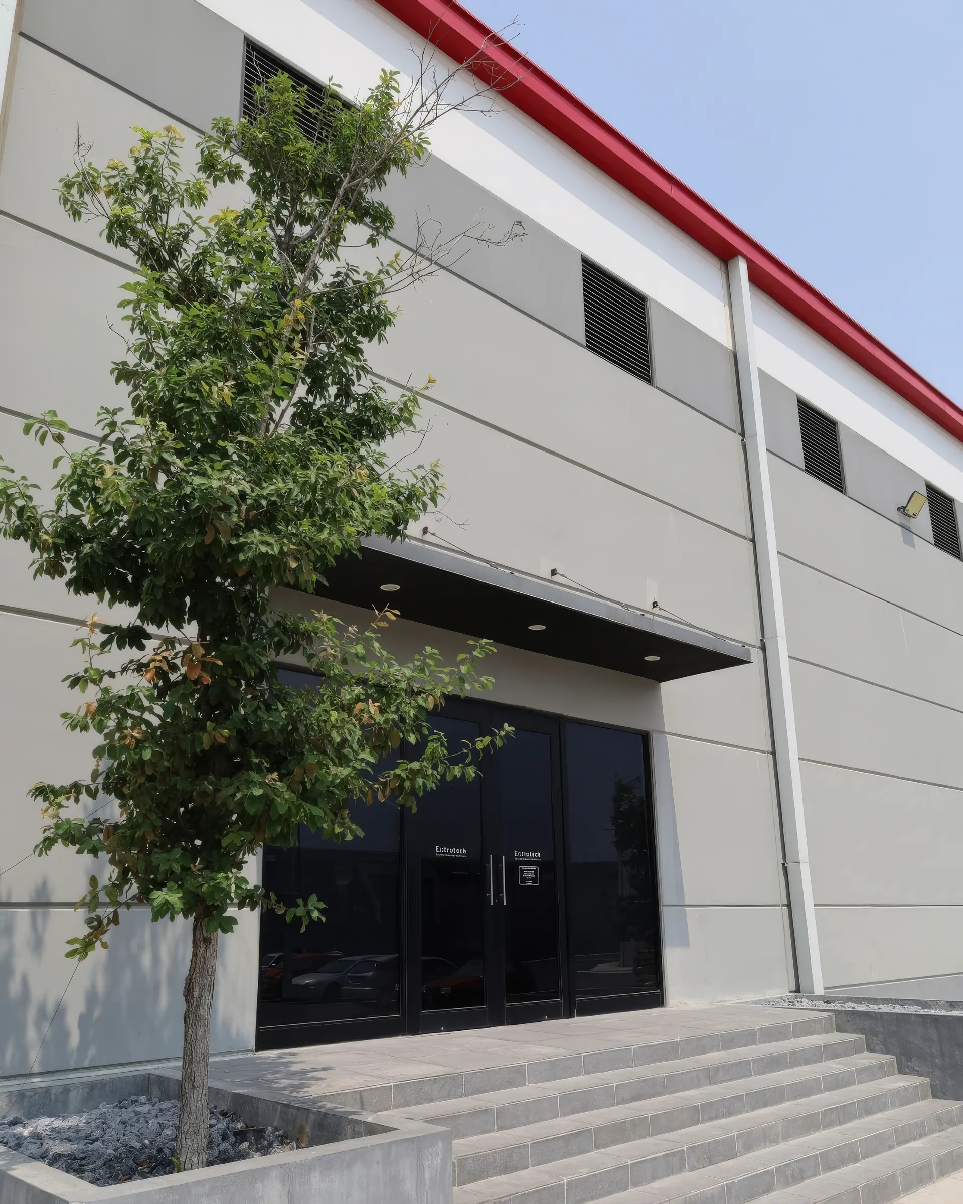 Fachada de la planta de Extrutech en Santa Catarina, Nuevo León: la nave gris con el acceso de cristal, la escalinata y un árbol al frente