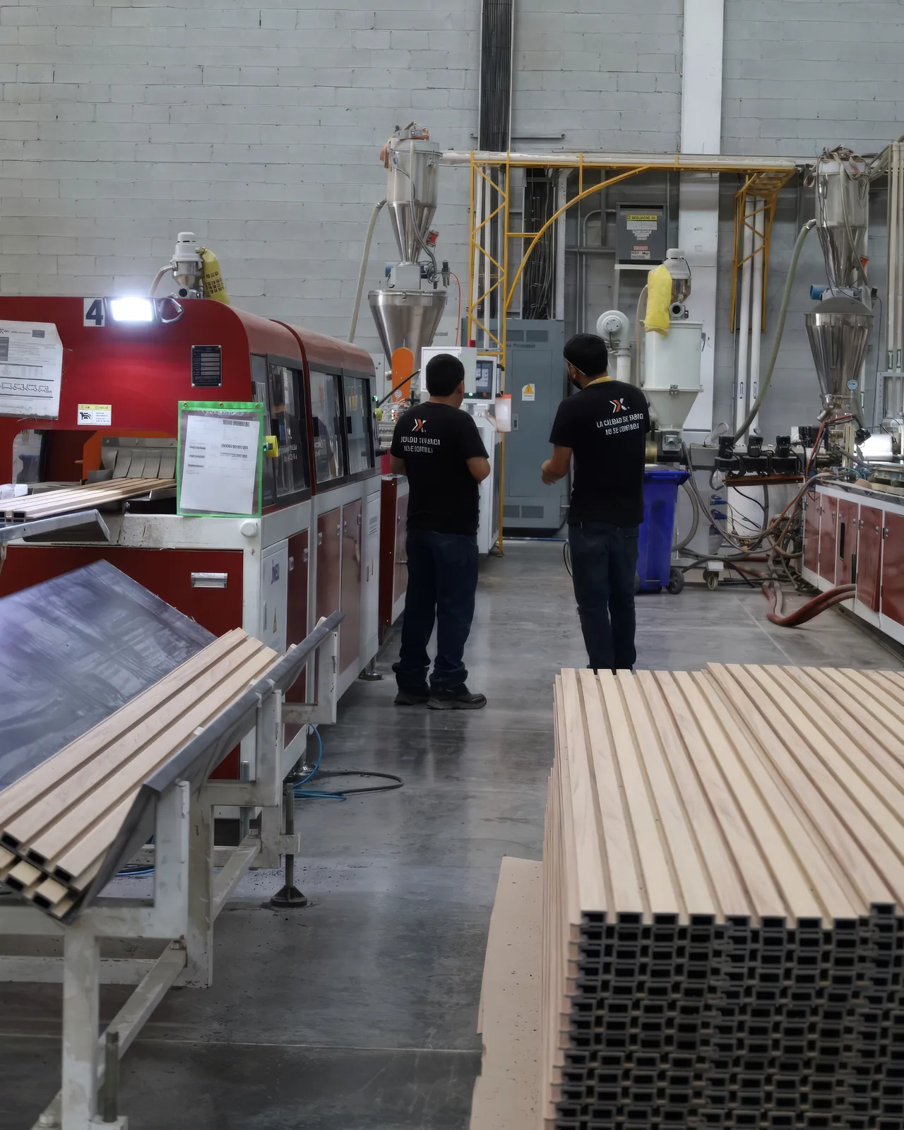 Dos operadores de Extrutech en la línea de extrusión de la planta, con una estiba de lambrín WPC en primer plano