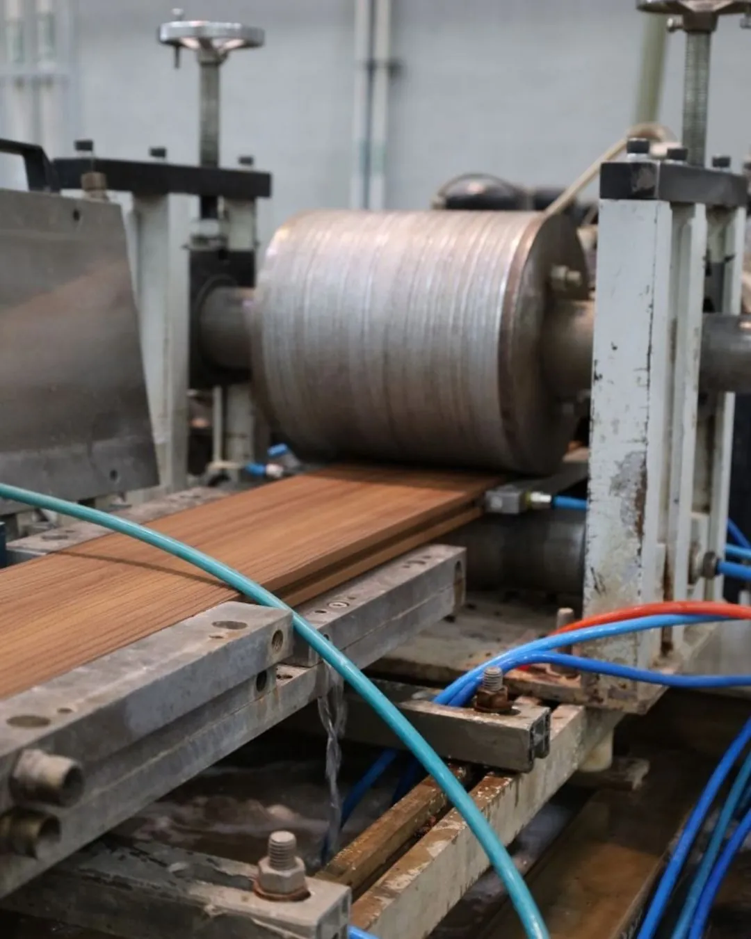 Tabla de deck WPC pasando bajo el rodillo que le estampa la veta en la línea de Extrutech
