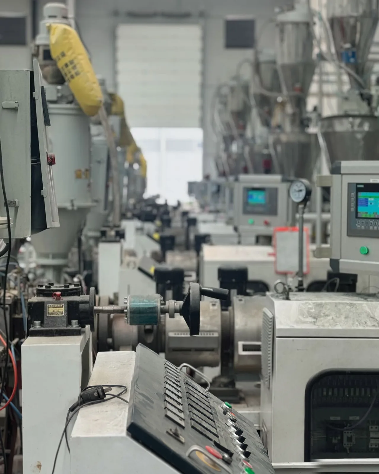 Hilera de extrusoras de la planta de Extrutech, con tableros de control, tolvas y la nave al fondo