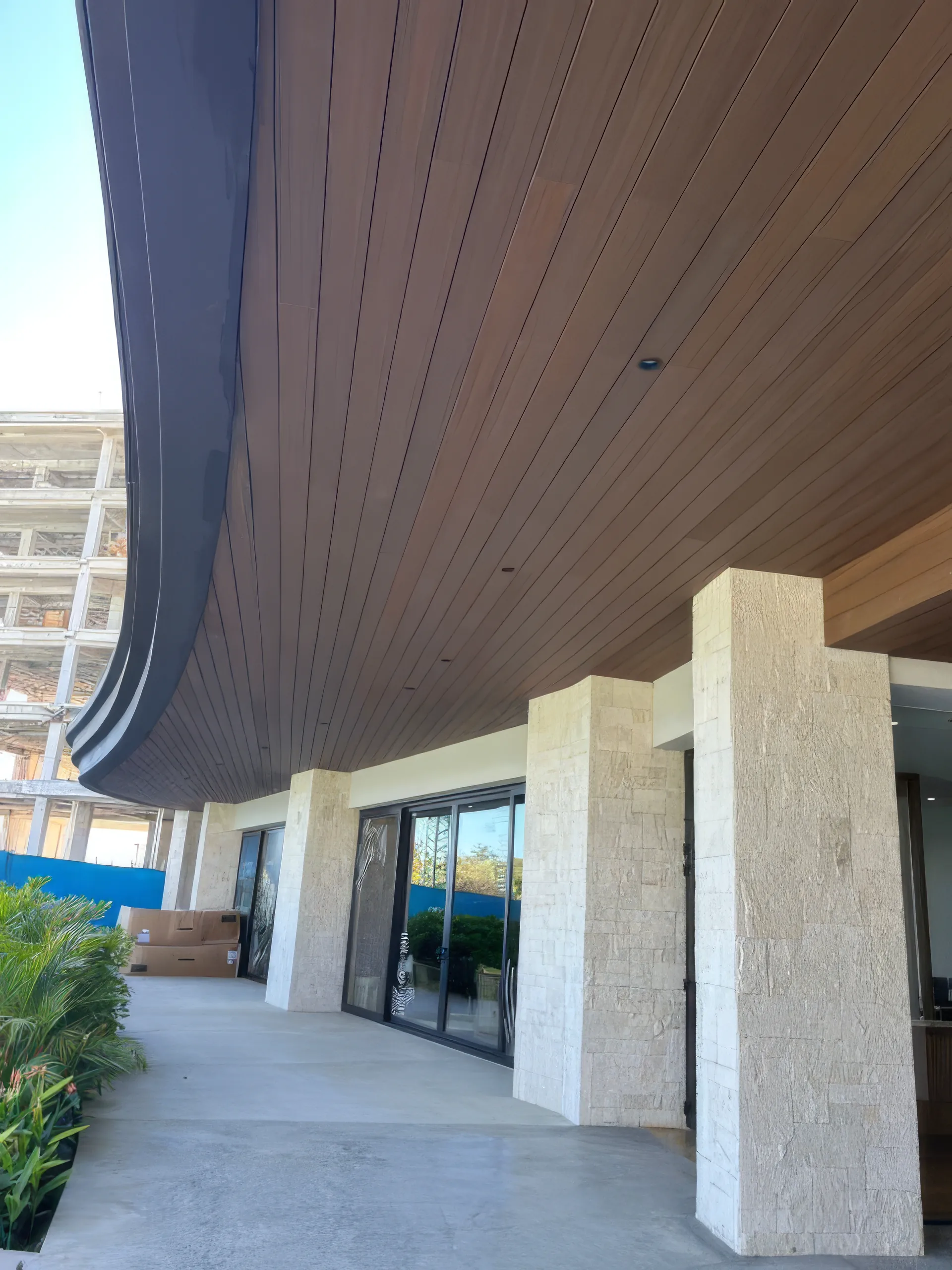 Techo exterior curvo forrado de Wall Cladding WPC en tono madera sobre columnas de piedra, en Kirah, Punta Mita
