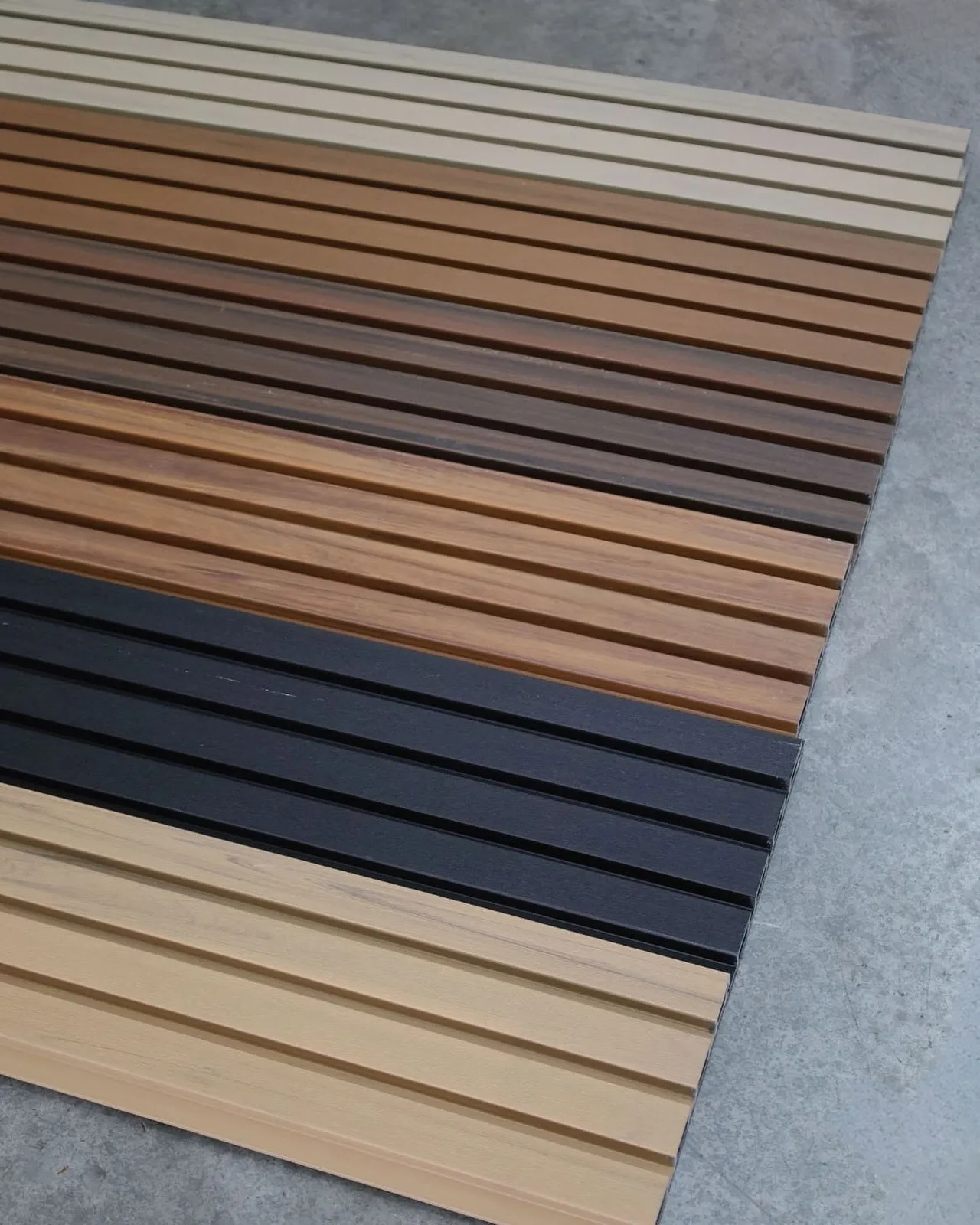 WPC grooved panel boards in several colors, laid side by side on a concrete floor