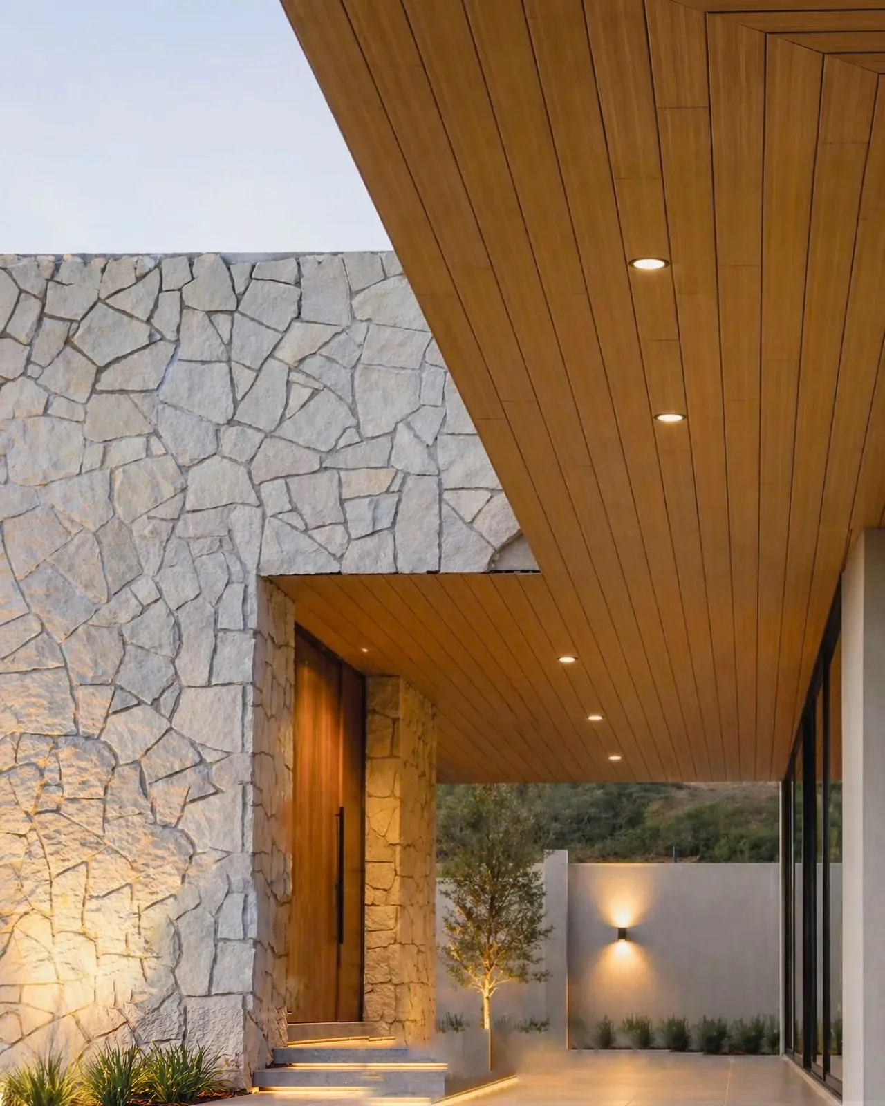 House entry porch at sunset with a WPC board ceiling and a stone wall