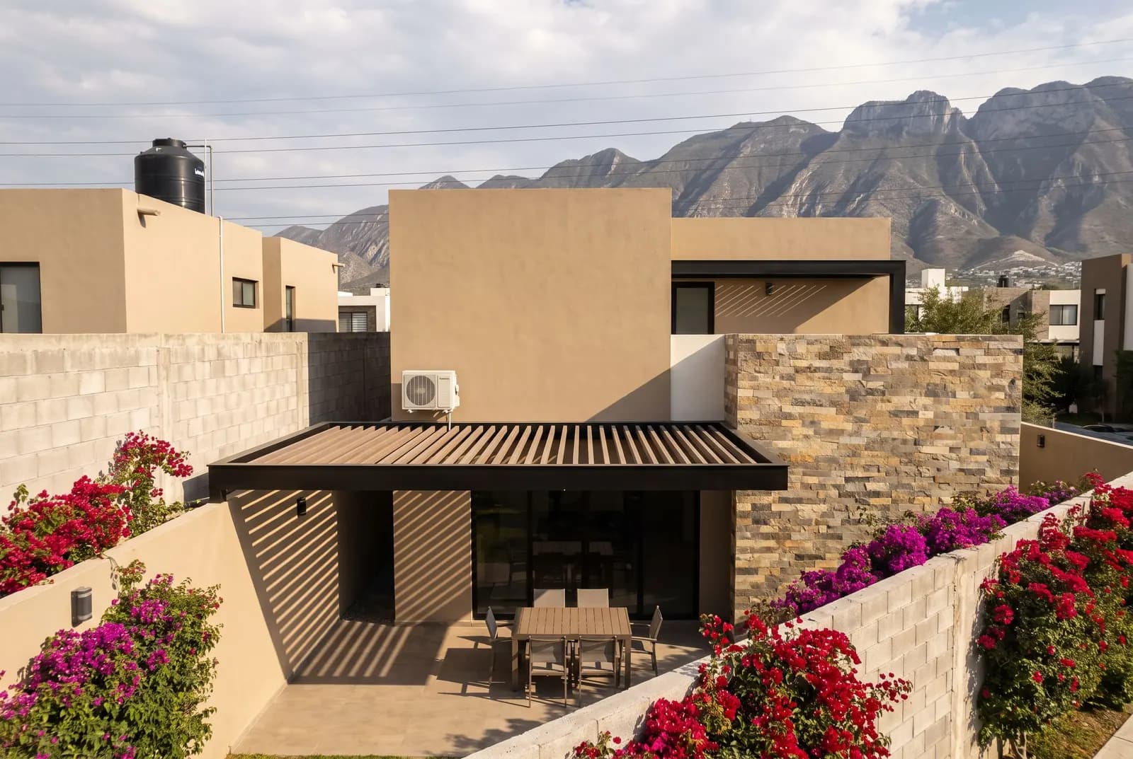House with a WPC beam pergola on the terrace and bougainvillea, with mountains in the background