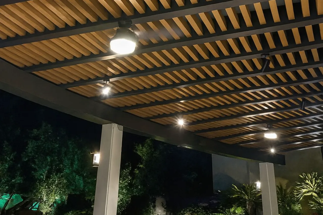 Pergola made of WPC decorative beams, lit at night, with a pendant light and a column