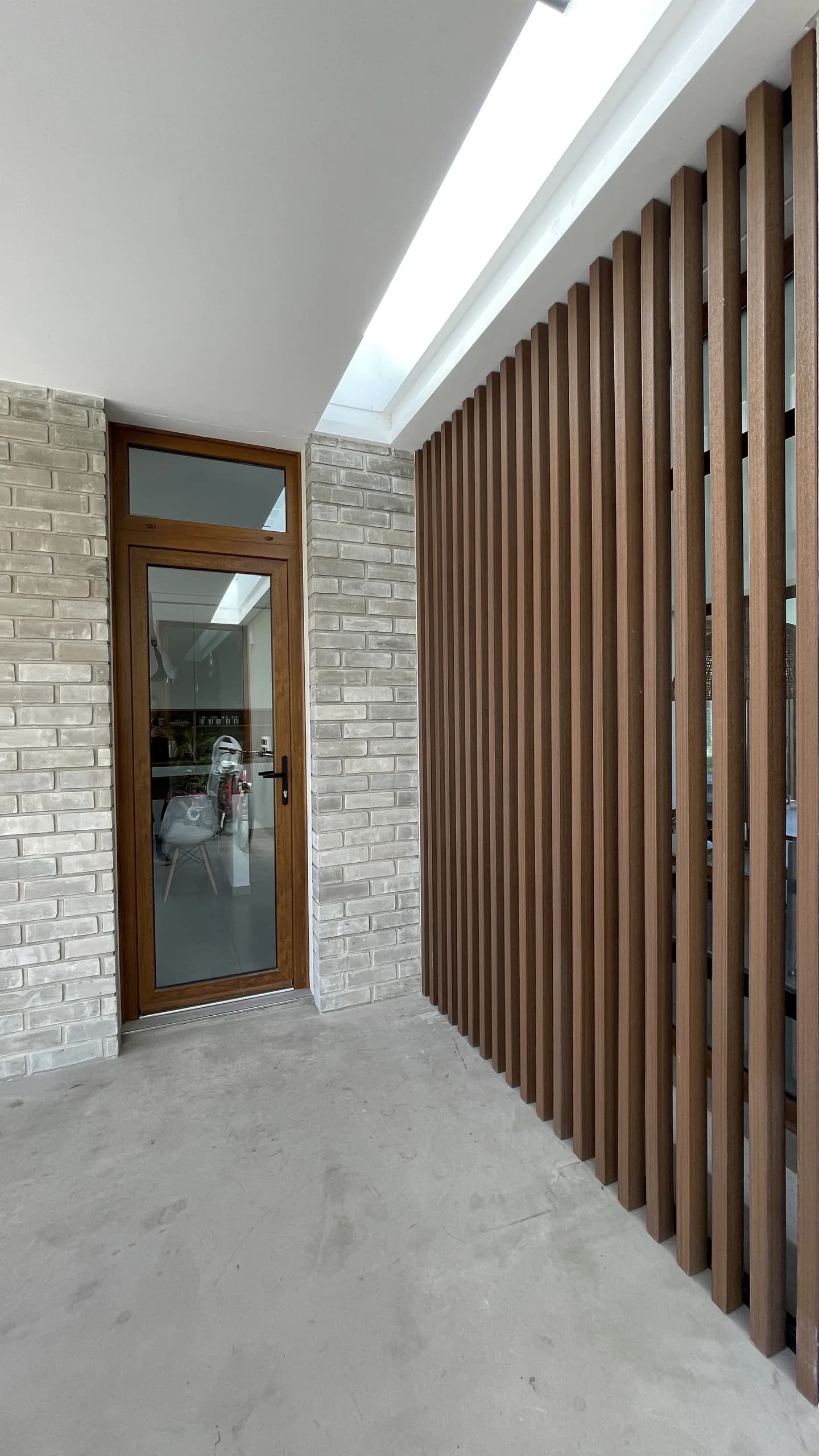 Screen of vertical wood-tone WPC decorative beams next to the front door of a house