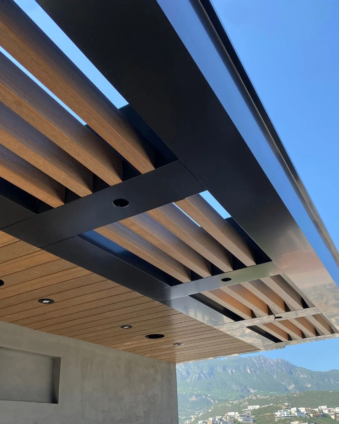 Pérgola de vigas decorativas WPC sobre un volado con Wall Cladding tono madera y luces empotradas, con la montaña al fondo
