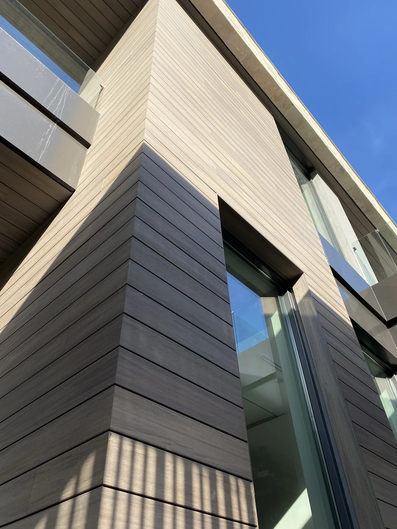 Corner of a facade clad in horizontal WPC boards, seen from below against a blue sky