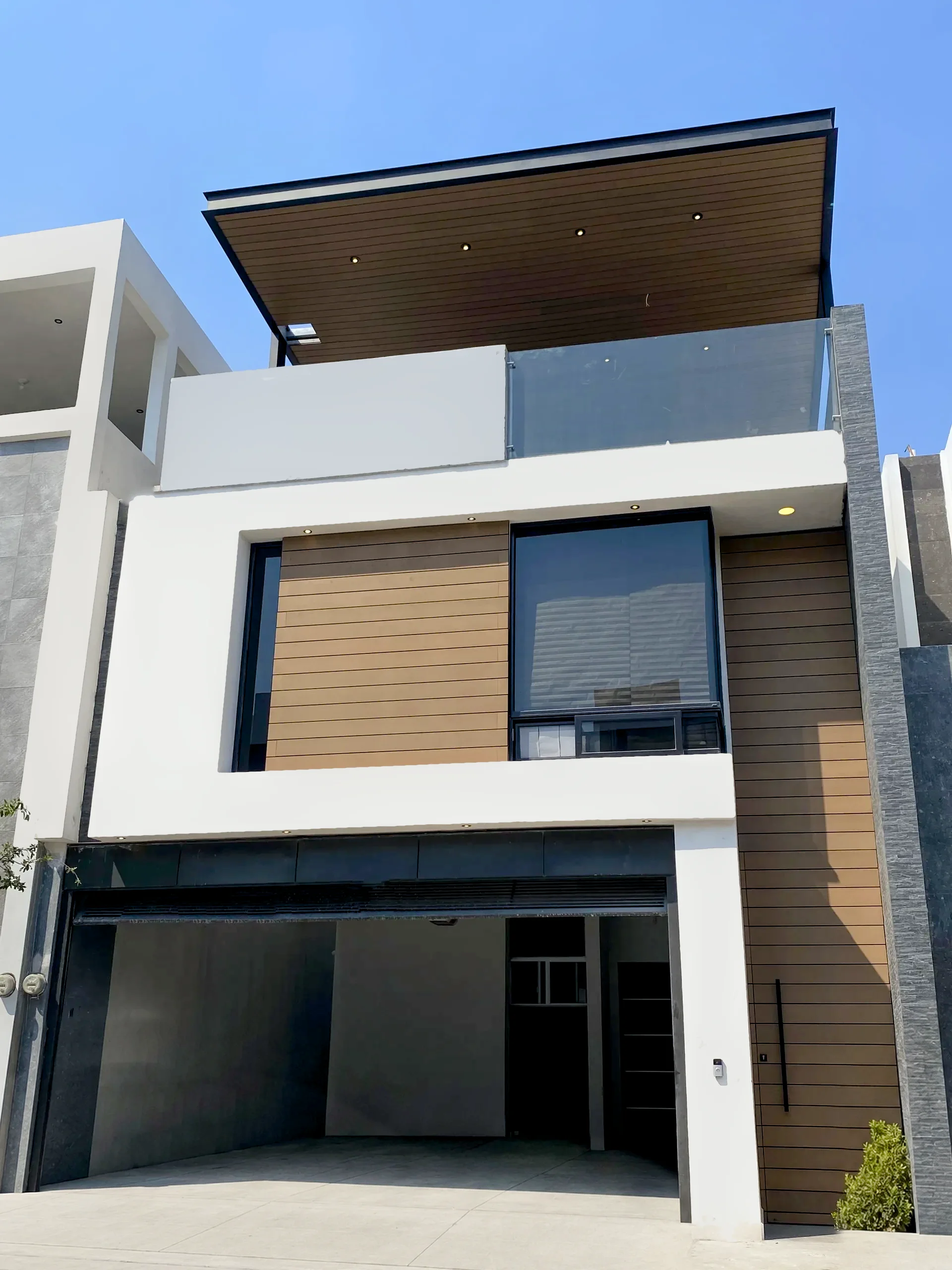 Three-story house facade with wood-tone WPC Wall Cladding in horizontal boards and a WPC soffit with recessed lights