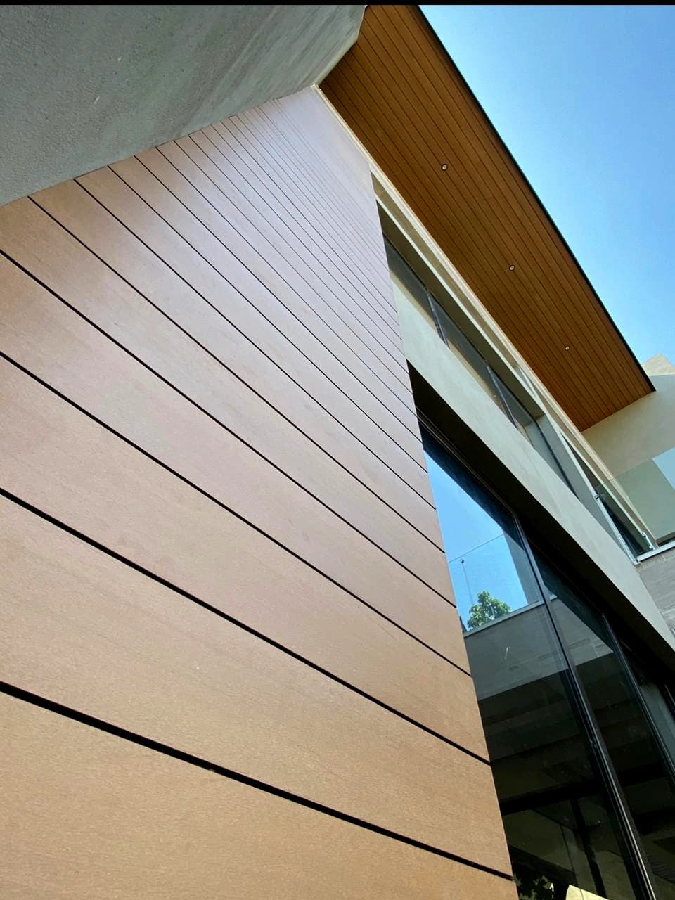 Exterior wall clad in horizontal boards of wood-tone WPC Wall Cladding, plus an overhang with a WPC soffit and recessed lights, seen from below