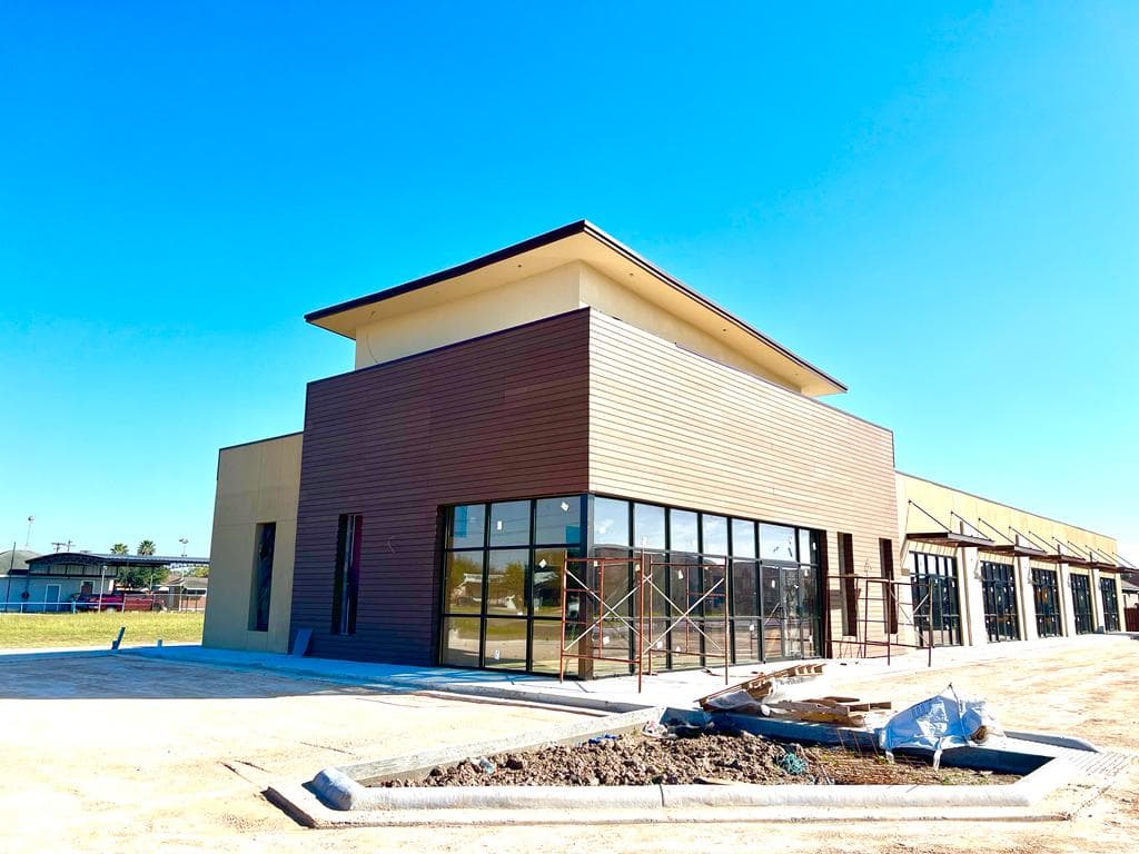 Commercial building under construction with its facade clad in wood-tone WPC Wall Cladding, under blue sky