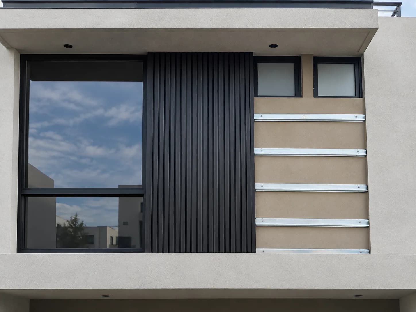 Fachada de una casa con canales listón horizontales fijados al muro junto a un tramo de lambrín WPC negro ya instalado en vertical
