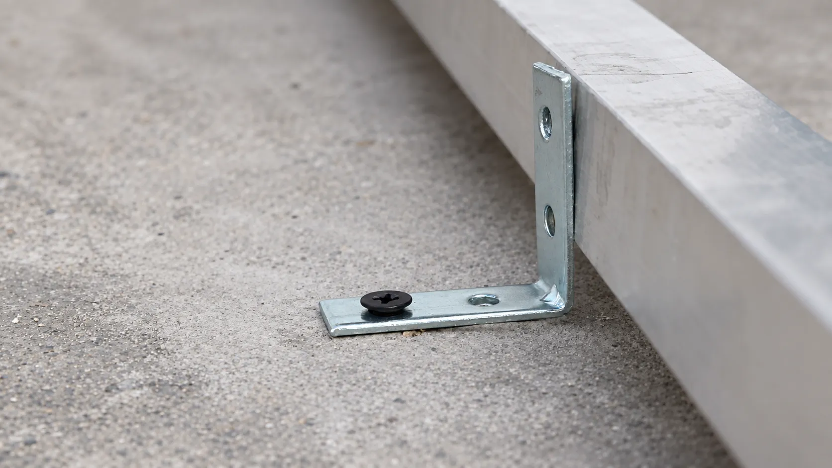 Escuadra atornillada al piso de concreto que sujeta un perfil de aluminio del bastidor