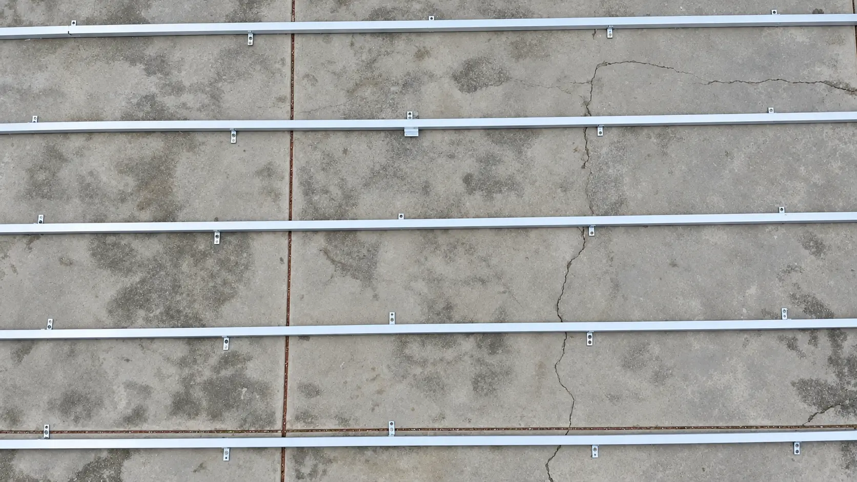 Perfiles de aluminio del bastidor alineados en paralelo sobre un piso de concreto, vistos desde arriba