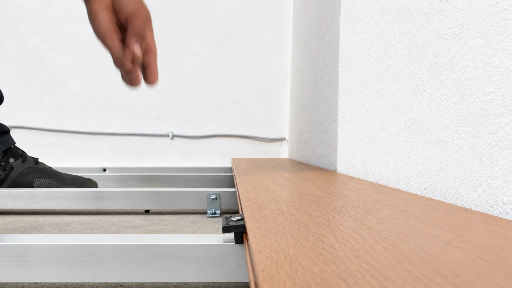 Primera tabla de deck WPC asentada sobre el bastidor de aluminio, junto al muro