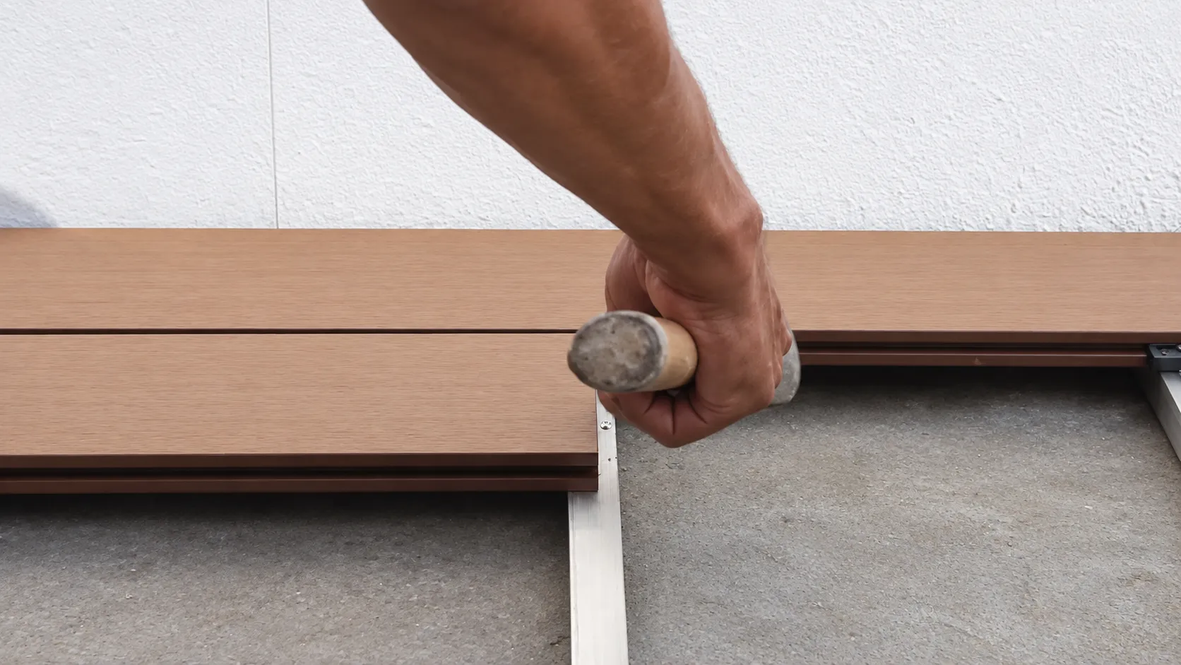 Instalador asienta una tabla de deck WPC con mazo de goma sobre el bastidor