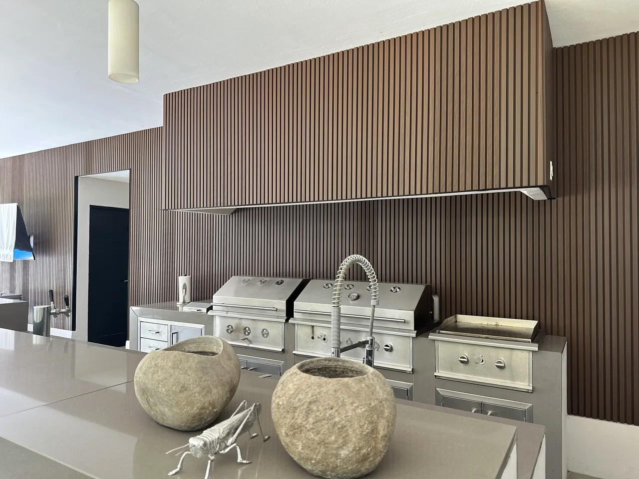 Outdoor kitchen with grills in front of a WPC grooved panel wall, with two stone planters on the counter