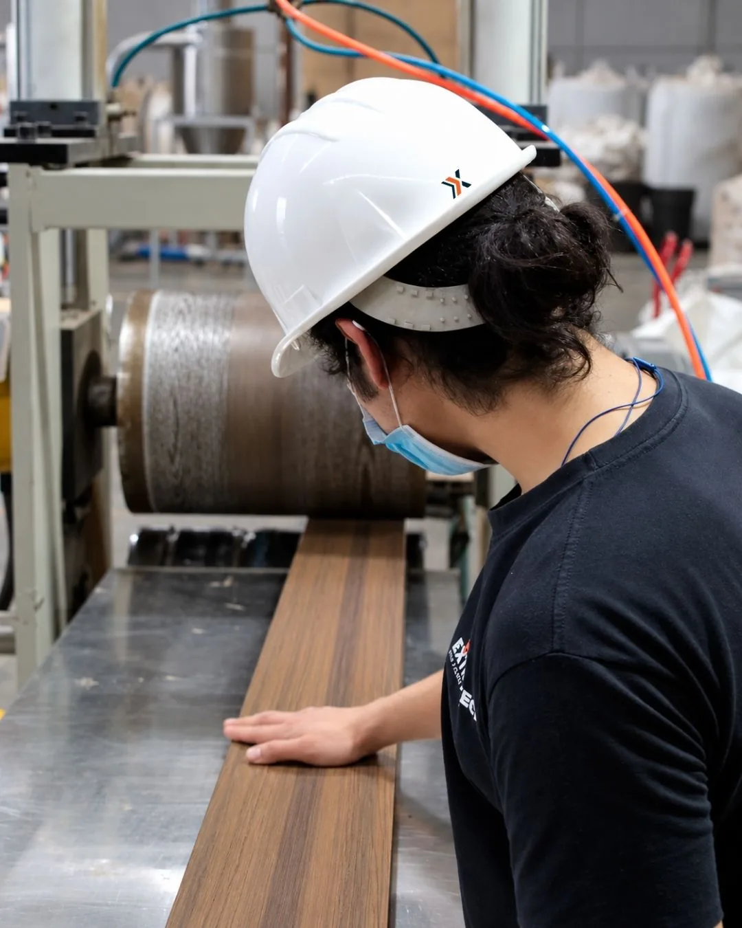 En la planta de Extrutech, un operador con casco y cubrebocas revisa una tabla de deck de WPC tono madera en la línea de producción