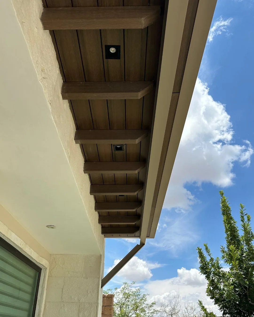 Alero de una casa con vigas WPC tono madera bajo el techo, visto desde abajo contra el cielo
